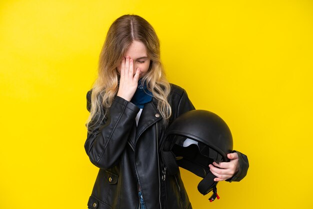 Una joven inglesa rubia con un casco de motocicleta aislado de fondo amarillo con expresión cansada y enferma