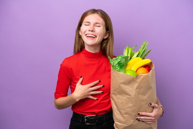 Joven inglesa sosteniendo una bolsa de compras aislada de fondo morado sonriendo mucho