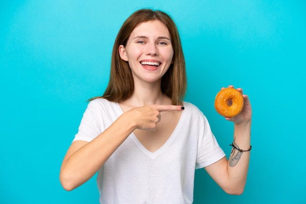 Joven inglesa sosteniendo un donut sobre un fondo azul aislado y apuntándolo