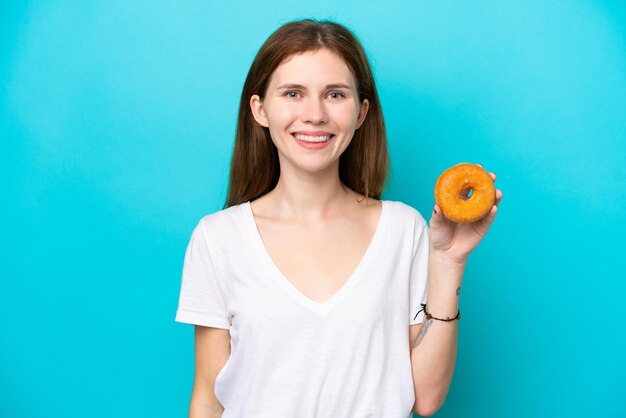 Joven inglesa sosteniendo un donut sobre un fondo azul aislado sonriendo mucho