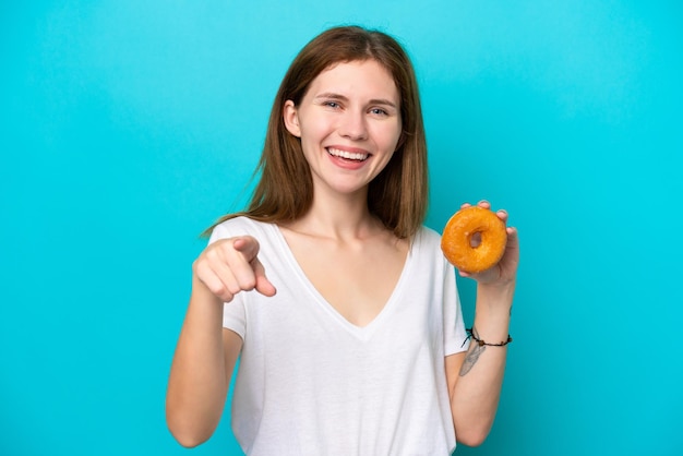 Una joven inglesa sosteniendo un donut sobre un fondo azul aislado te señala con una expresión de confianza