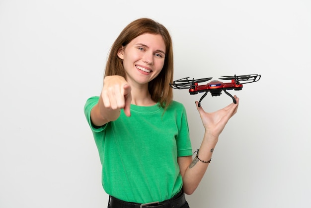 Joven inglesa sosteniendo un dron aislado de fondo blanco apuntando al frente con expresión feliz