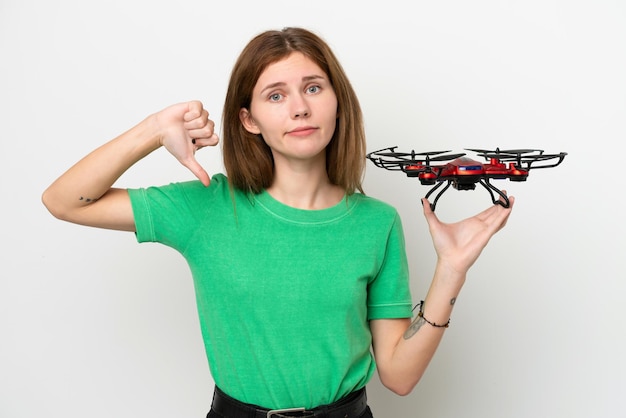 Foto joven inglesa sosteniendo un dron aislado de fondo blanco mostrando el pulgar hacia abajo con expresión negativa