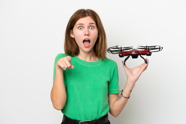 Joven inglesa sosteniendo un dron aislado de fondo blanco sorprendida y apuntando al frente