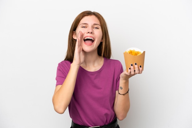 Joven inglesa sosteniendo patatas fritas aisladas de fondo blanco gritando con la boca abierta