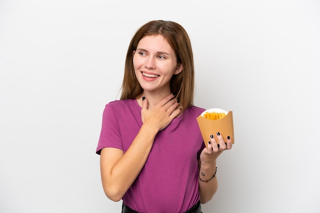 Joven inglesa sosteniendo patatas fritas aisladas de fondo blanco mirando hacia arriba mientras sonríe