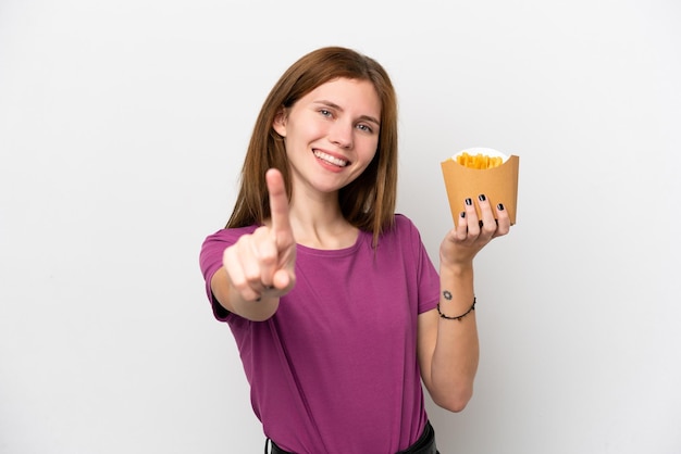 Joven inglesa sosteniendo patatas fritas aisladas de fondo blanco mostrando y levantando un dedo