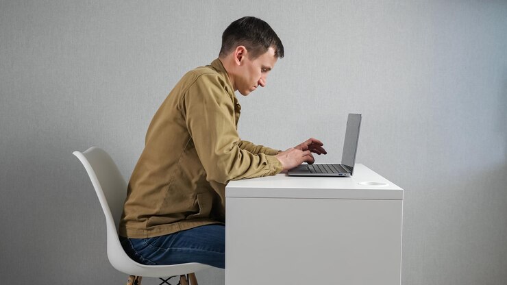 Foto joven se inquieta en la silla trabajando a través de una computadora portátil en la mesa
