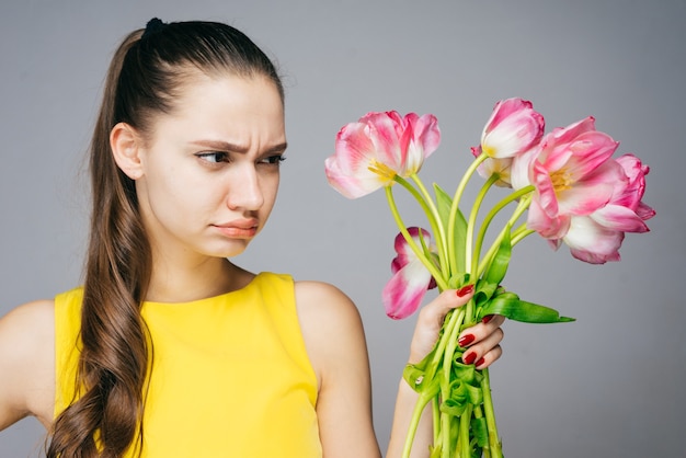 Joven insatisfecha en vestido amarillo tiene flores fragantes en las manos