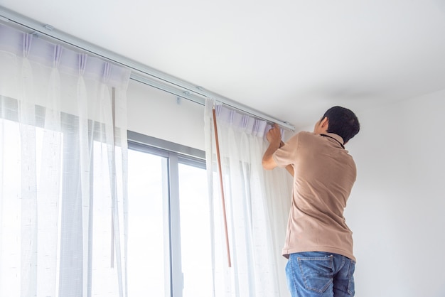 Joven instalando cortinas ciegas sobre ventana en renovar dentro de la casa.