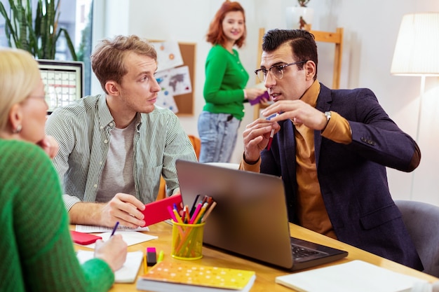 Joven inteligente sentado frente a la computadora portátil mientras comparte conocimientos con sus colegas