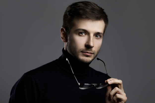 Joven inteligente vestido con cuello alto y anteojos sobre fondo gris