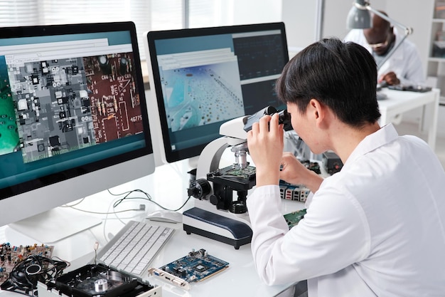 Joven investigadora asiática mirando en microscopio