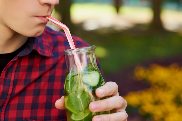 Joven irreconocible bebe té de desintoxicación saludable con jugo en el fondo del parque verde.