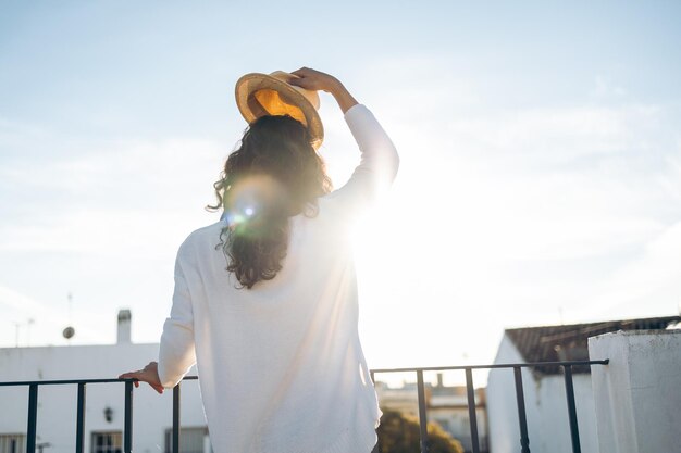 Joven irreconocible quitándose el sombrero en un día soleado en la azotea