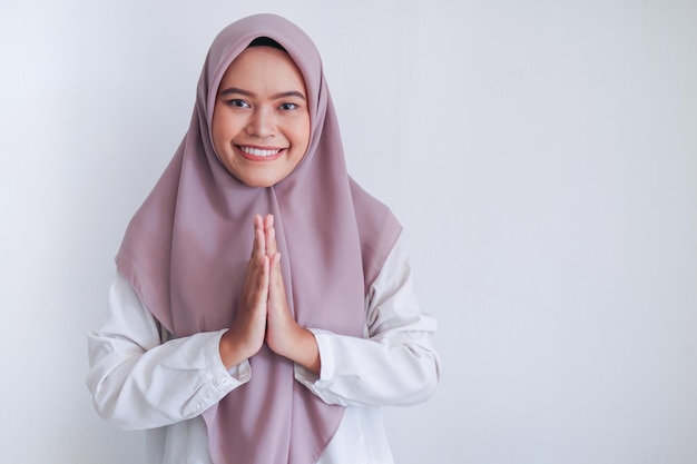 Una joven islámica asiática con velo saluda con una gran sonrisa en su rostro Mujer indonesia de fondo gris Saludo de Eid Mubarak