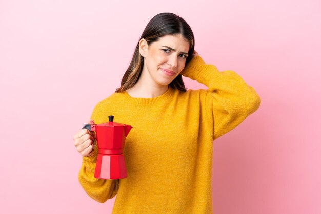 Joven italiana sosteniendo una cafetera aislada de fondo rosa con dudas