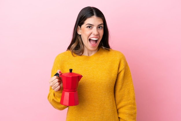 Joven italiana sosteniendo una cafetera aislada de fondo rosa con expresión facial sorpresa