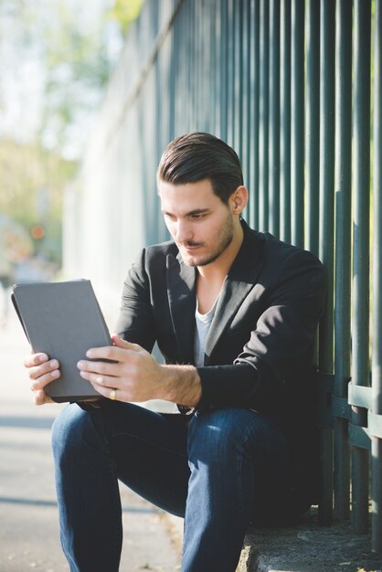 Joven italiano sentado en una acera con tableta