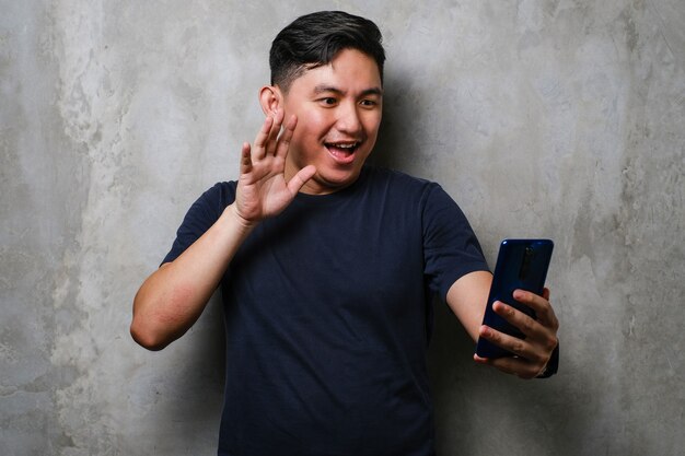 Joven japonés sonriendo feliz haciendo videollamadas con smartphone sobre fondo de pared de hormigón