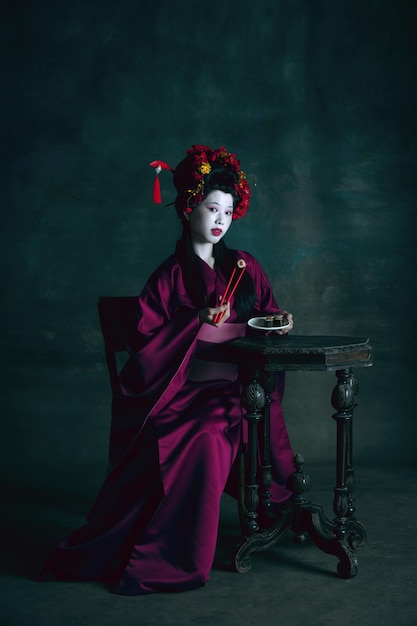 Joven japonesa como geisha en pared verde oscuro