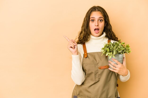 Joven jardinero caucásico mujer sosteniendo una planta aislada apuntando hacia el lado