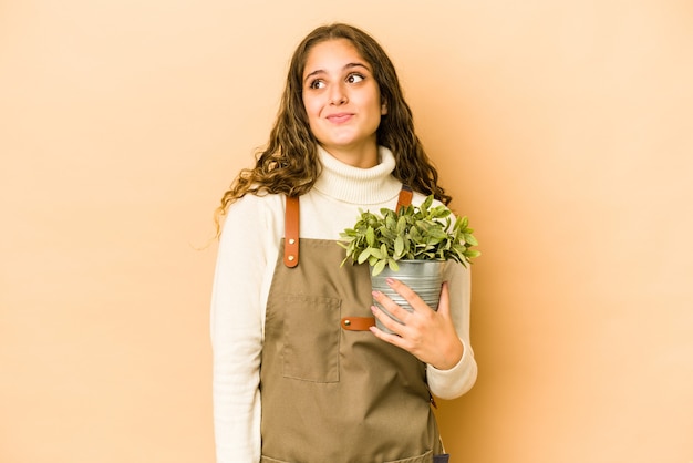 Joven jardinero caucásico mujer sosteniendo una planta aislada soñando con lograr metas y propósitos