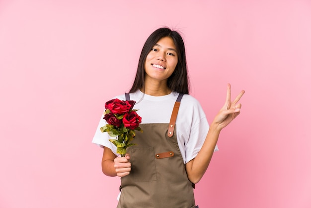 Joven jardinero chino mujer sosteniendo un rosas aislado alegre y despreocupado mostrando un símbolo de paz con los dedos