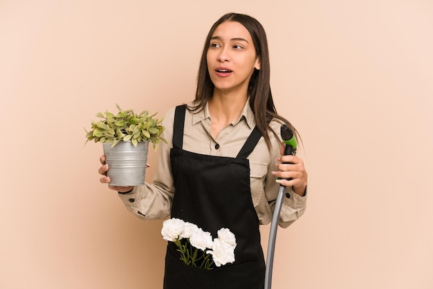 Joven jardinero colombiano sostiene una planta y una manguera, nutriendo la naturaleza.