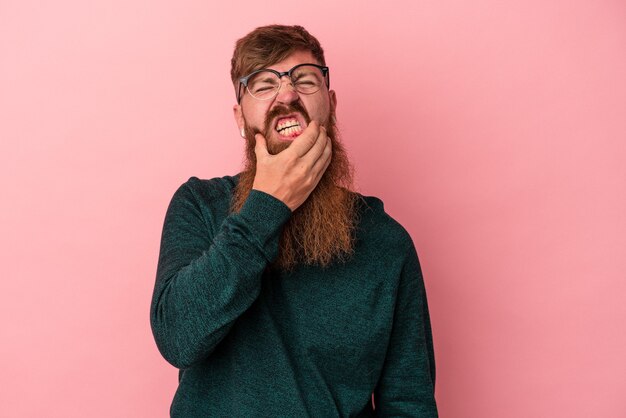 Joven jengibre caucásico con barba larga aislado sobre fondo rosa con un fuerte dolor de dientes, dolor molar.