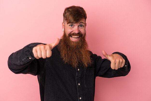 Foto joven jengibre caucásico con barba larga aislado sobre fondo rosa levantando ambos pulgares, sonriente y confiado.