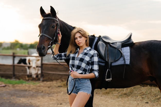 Un joven jinete de niña bonita posa cerca de un semental de pura sangre en un rancho. Equitación, carreras de caballos.