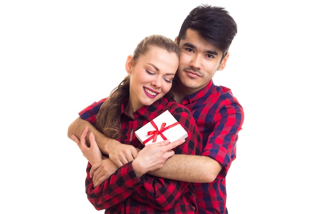 Joven y joven mujer feliz con un pequeño regalo blanco vistiendo camisas a cuadros rojas abrazándose