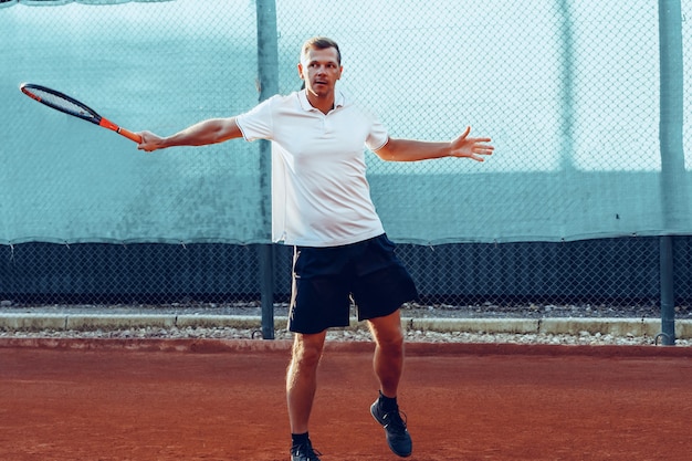 Joven juega al tenis al aire libre en la cancha de tenis por la mañana