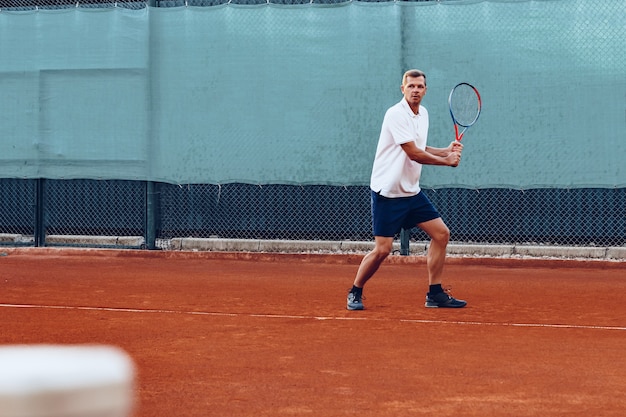 Joven juega al tenis al aire libre en la cancha de tenis por la mañana