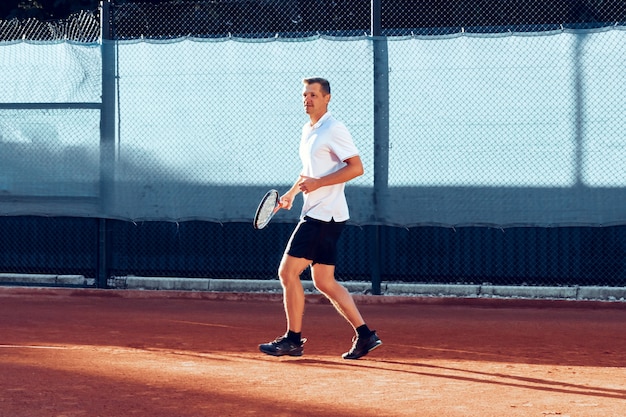 Joven juega al tenis al aire libre en la cancha de tenis de tierra batida en la mañana