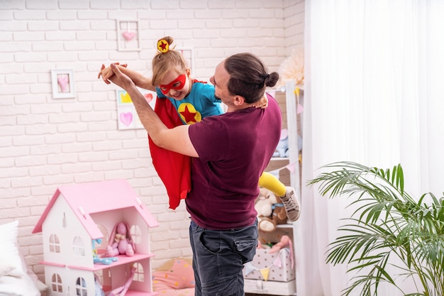 Joven juega con su hija en superhéroes en la sala.