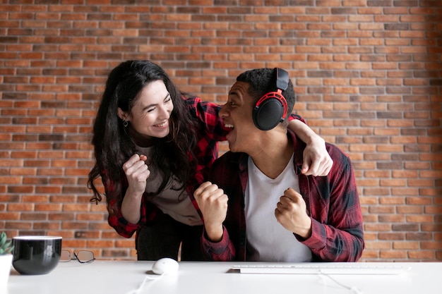 Joven jugador afroamericano en auriculares con chica se regocija en la victoria juntos en la mesa de la computadora