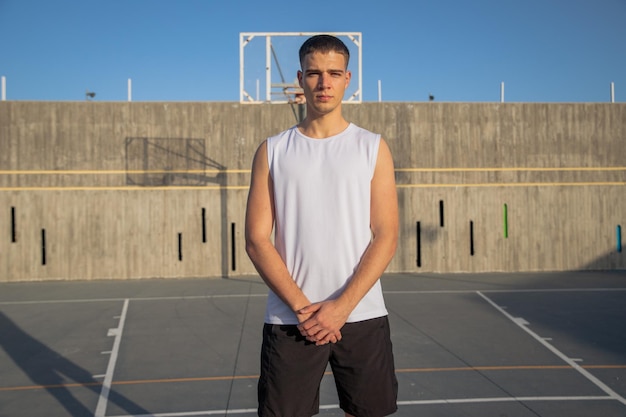 Un joven jugador de baloncesto en una cancha de baloncesto se toma las manos y tiene una expresión de confianza.