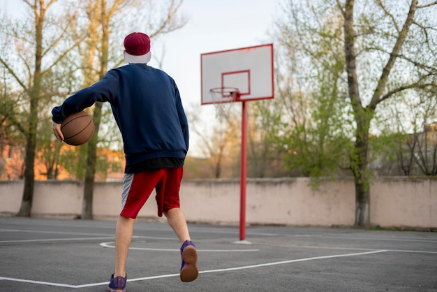 Joven jugador de baloncesto entrenando para driblar al aire libre en la cancha de asfalto