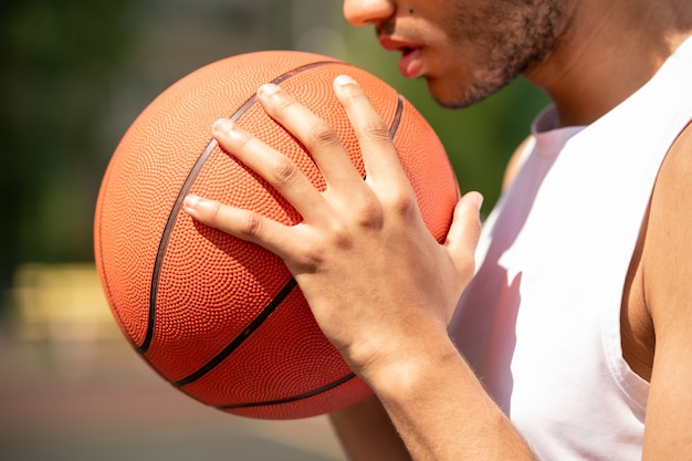 Joven jugador de baloncesto masculino contemporáneo sosteniendo la pelota por la cara y el pecho mientras se prepara para pasar