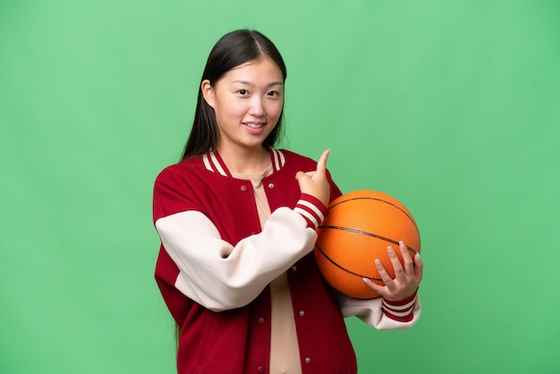 Joven jugador de baloncesto mujer asiática sobre fondo aislado apuntando hacia atrás