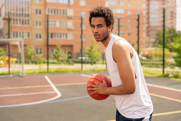 Joven jugador de baloncesto sosteniendo la pelota por el pecho mientras apunta a tirarla a la canasta durante el entrenamiento