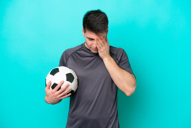 Joven jugador de fútbol caucásico aislado de fondo azul con expresión cansada y enferma