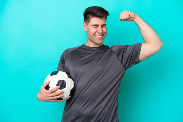 Joven jugador de fútbol caucásico aislado de fondo azul haciendo un gesto fuerte