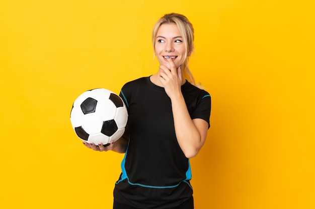 Joven jugador de fútbol ruso mujer aislada en amarillo mirando hacia arriba mientras sonríe