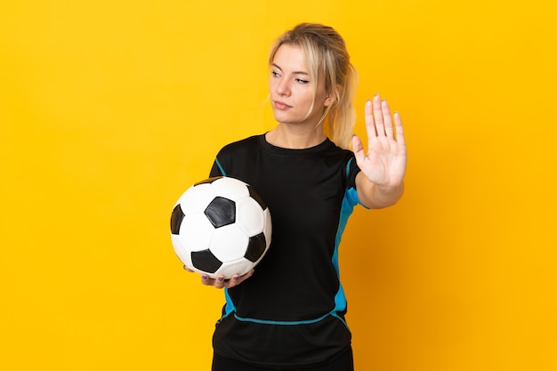 Joven jugador de fútbol ruso mujer aislada en la pared amarilla haciendo gesto de parada y decepcionado