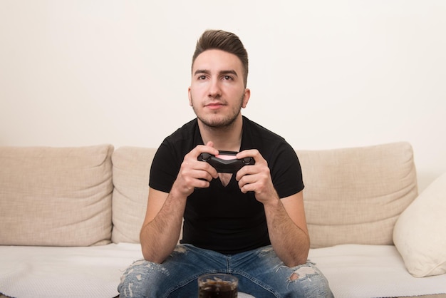 Joven jugador sentado en el sofá y jugando videojuegos en casa