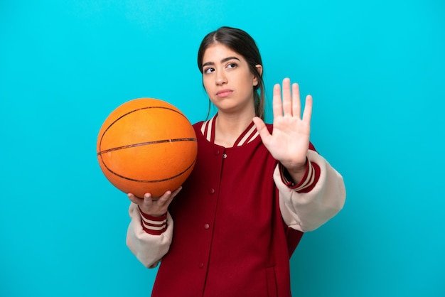 Joven jugadora de baloncesto caucásica aislada de fondo azul haciendo un gesto de parada y decepcionada