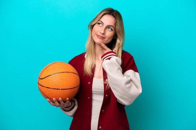 Una joven jugadora de baloncesto caucásica aislada de fondo azul mirando hacia arriba mientras sonríe